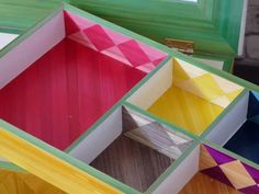 four different colored boxes sitting next to each other on top of a wooden table with a window in the background