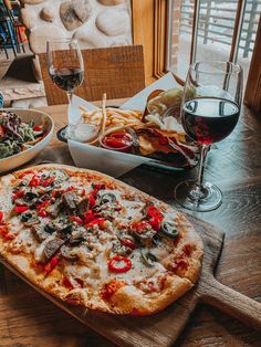 a pizza sitting on top of a wooden cutting board next to a glass of wine