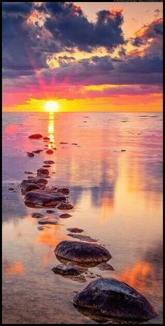 the sun is setting over some rocks in the water