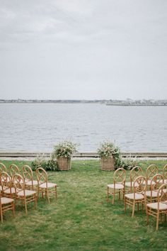 an outdoor ceremony set up with chairs and flower baskets in front of the water's edge