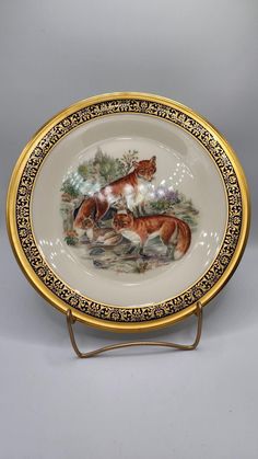 a plate with two cats on it sitting in front of a gray background and gold trim around the edge