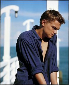 a young man leaning against a railing near the ocean with his hands on his hips