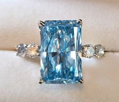 Gorgeous brilliant cut 8.59ct lab grown blue diamond ring bookended by .8ctw natural diamonds. Center lab grown diamond: Cut Cornered Rectangular Modified Brilliant 15.74x10.2x6.01mm SI1-SI2 Clarity Side natural diamonds: round brilliant cut 3.8 mm approximate .8ctw color H-J clarity I1-I2 Ring: 14ct white gold out of roundGorgeous brilliant cut 8.59ct lab grown blue diamond ring bookended by .8ctw natural diamonds. Center lab grown diamond: Cut Cornered Rectangular Modified Brilliant 15.74x10.2 Blue Diamond Ring With Diamond Accents Emerald Cut, Blue Emerald Cut Diamond Ring With Diamond Accents, Blue Emerald Cut Diamond Ring With Accents, Luxury Blue Radiant Cut Diamond Ring, Blue Asscher Cut Diamond Ring With Accents, Blue Radiant Cut Diamond Jewelry, Gia Certified Blue Radiant Cut Jewelry, Blue Radiant Cut Diamond Accented Jewelry, Blue Radiant Cut Cubic Zirconia Rings