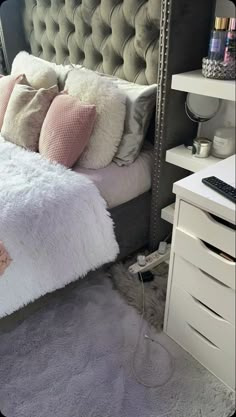 a bed with white and pink pillows on top of it next to a night stand