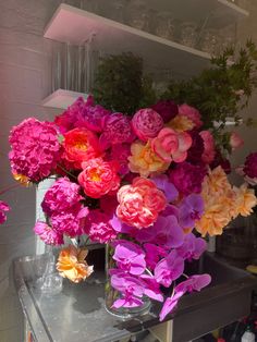 a vase filled with lots of pink and orange flowers on top of a table next to a shelf