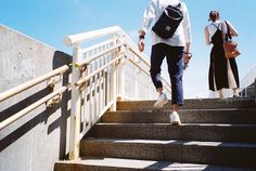 two people walking up some stairs with bags on their backs and one person carrying a backpack