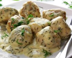 a white plate topped with meatballs covered in gravy and garnished with herbs