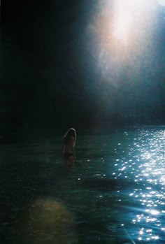 a woman standing in the middle of a body of water with her back turned to the camera