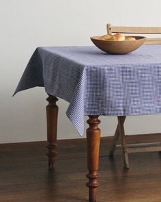 a bowl of food on top of a wooden table next to a bench with a blue gingham cloth