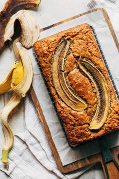 a loaf of banana bread sitting on top of a cutting board next to two bananas