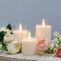 three white candles sitting on top of a table next to flowers and lace doily