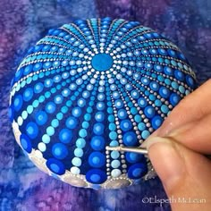 a person is painting on a rock with blue and white dots