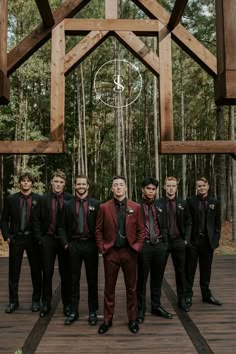 a group of men standing next to each other in front of a wooden structure and trees