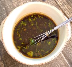 a white bowl filled with soup on top of a wooden table next to a whisk