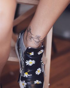 a woman's foot with daisies tattooed on the side of her shoe, while sitting in a chair