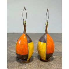 two orange and yellow vases sitting on top of a cement floor next to each other