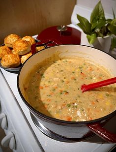 a pot filled with soup next to muffins on top of a stovetop