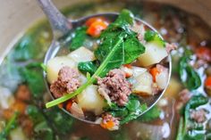 a ladle full of soup with meat, potatoes and spinach in it is being held by a spoon