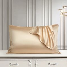 a white dresser with a beige pillow on top of it and a lamp in the background