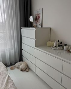 a dog laying on the floor in front of a dresser with drawers and other items