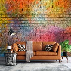 a brown leather couch sitting in front of a brick wall with colorful paint on it