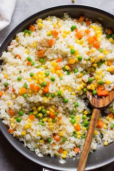 rice with peas and carrots in a skillet on top of a table next to a wooden spoon