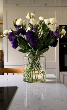 a vase filled with purple and white flowers on top of a kitchen counter next to an oven