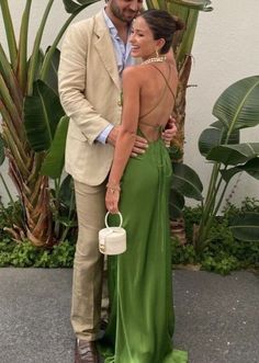 a man and woman standing next to each other in front of some palm trees wearing green dresses