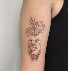 a woman with a tattoo on her arm has a vase with flowers and leaves in it