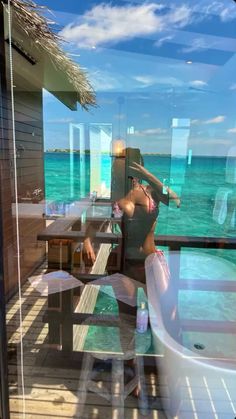 a woman standing in front of a window next to the ocean