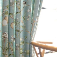 a chair sitting in front of a window covered in blue curtains with birds and flowers on them