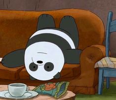 a cartoon panda bear laying on top of a couch next to a cup and saucer