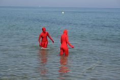 two people in red body suits walking into the ocean