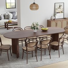 a dining room table with chairs and fruit on the table in front of it, next to a couch