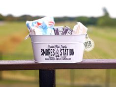 a white bucket filled with candy sitting on top of a wooden rail next to a field