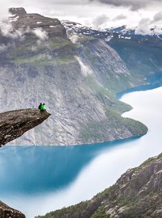 a man standing on top of a cliff next to a lake