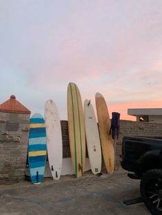 several surfboards are lined up against the wall in front of a pickup truck at sunset