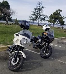 two motorcycles parked next to each other in a parking lot near the water and trees