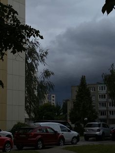 several cars parked on the side of a road in front of tall buildings with dark clouds overhead