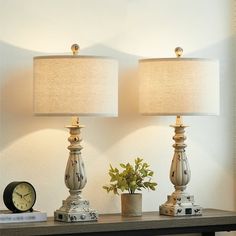 two lamps sitting on top of a wooden table next to a clock and potted plant