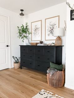 a black dresser sitting in the corner of a room next to a white door and potted plant