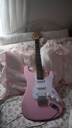 a pink electric guitar sitting on top of a bed next to pillows and a pillow