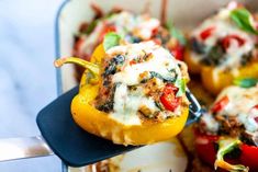 stuffed bell peppers with cheese and spinach in a casserole dish being held by a spatula