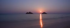 the sun is setting over two small rocks in the middle of the ocean with reflections on the water