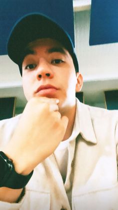 a young man wearing a baseball cap and looking at the camera with his hand on his chin