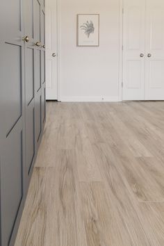 an empty room with wooden floors and white walls, framed pictures on the wall above them