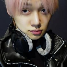 a man with pink hair wearing headphones and a leather jacket is looking at the camera