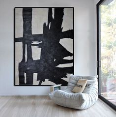 an abstract painting hangs on the wall next to a modern chair in front of a large window