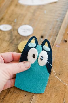 someone is making a felt owl decoration on the wooden table with other buttons and thread