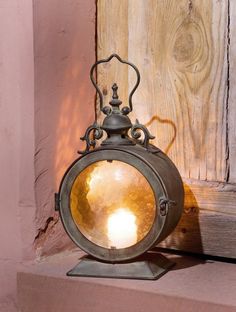 an old fashioned lantern with two lit candles on it's stand next to a wooden wall